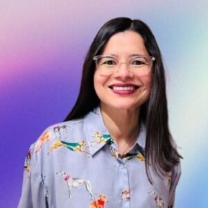 Portrait of international SEO consultant and author Aleyda Solis smiling in clear glasses and a dog-patterned collared shirt against a purple-to-blue gradient backdrop.