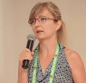 Digital marketer and SEO specialist Ann Smarty speaking into a handheld microphone with eyeglasses and a conference lanyard.