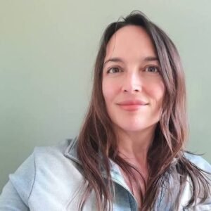 Headshot portrait of link building specialist Bibi Raven smiling softly in a denim jacket against a muted green wall."