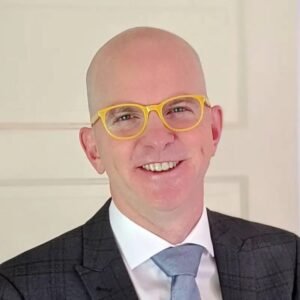 Headshot portrait of SEO consultant and Zyppy founder Cyrus Shepard smiling in bright yellow glasses, a dark plaid suit jacket, and a blue tie