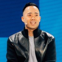Portrait of digital marketing entrepreneur and podcaster Eric Siu smiling on stage wearing a black bomber jacket and a discreet headset microphone.