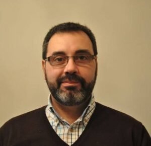 Headshot portrait of international SEO consultant Gianluca Fiorelli wearing black rectangular glasses and a white button-down shirt against a gray background.