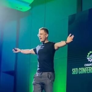 Affiliate SEO expert Matt Diggity speaking on stage with open arms at Chiang Mai SEO Conference under green stage lighting.