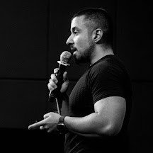 Black-and-white side profile of holistic SEO expert Koray Tuğberk Gübür speaking into a microphone on stage.