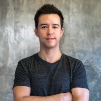 Headshot portrait of affiliate SEO entrepreneur and speaker Matt Diggity smiling with arms crossed in a dark gray t-shirt against a textured concrete wall.