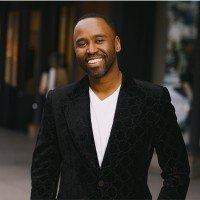 Portrait of digital marketing executive and SEO technologist Mike King smiling in a black patterned blazer and white v-neck shirt.